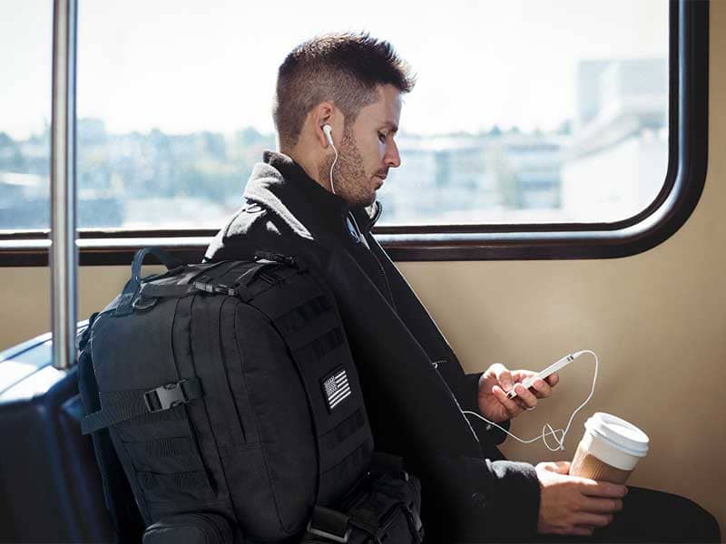 A man is listening to music with a backpack on his back in the train carriage.