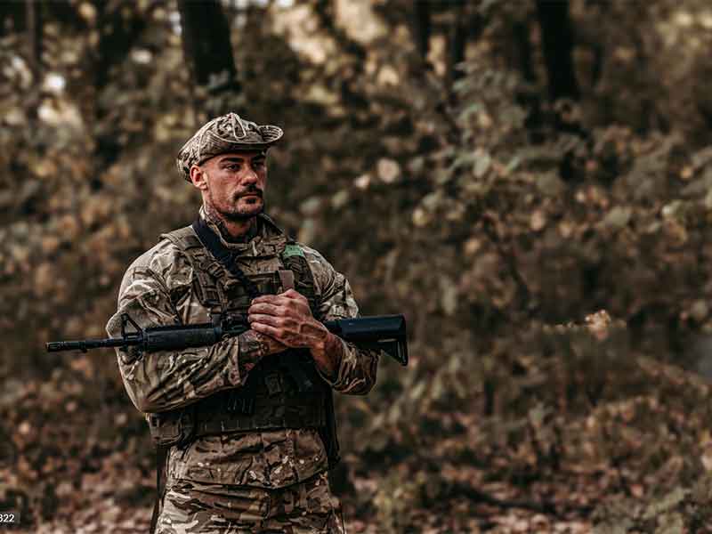 Soldier wearing camouflage boonie hat and tactical vest in woodland environment