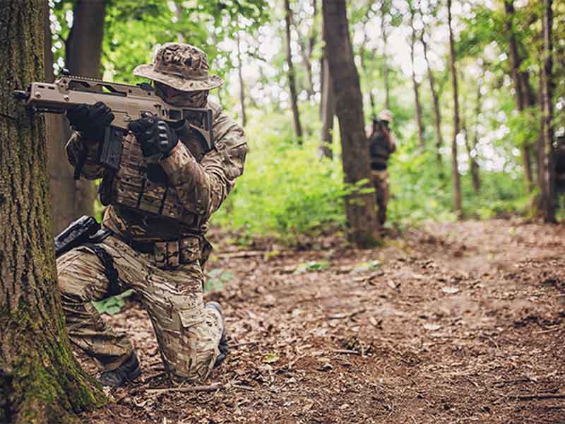 Soldier in boonie hat aiming during woodland tactical training