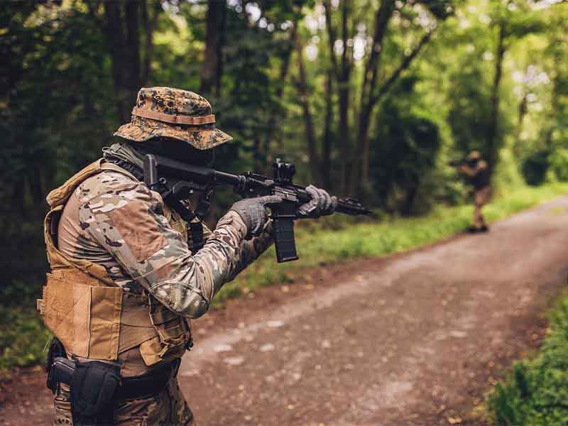 Camouflage soldier with boonie hat and tactical gear on forest road mission