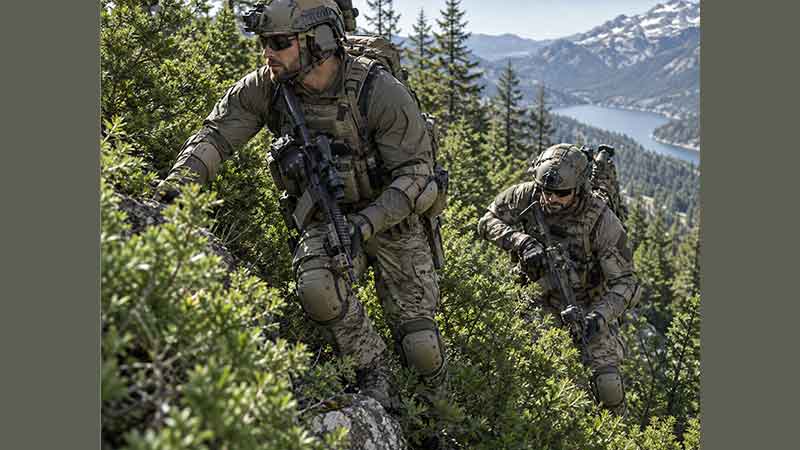 Tactical soldiers wearing knee and elbow pads during mountain field training with full combat gear.